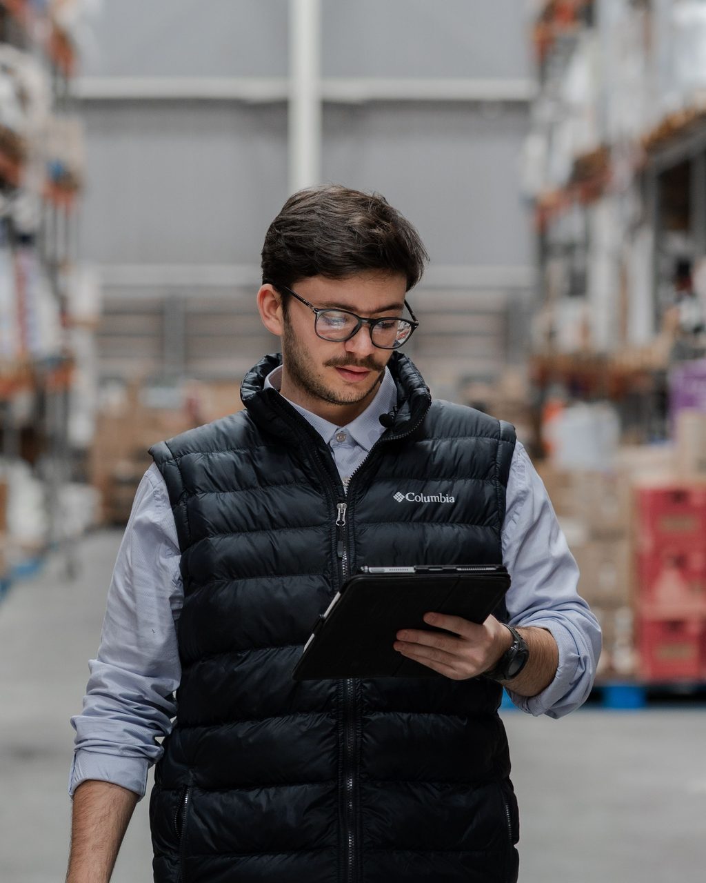 Young male in warehouse checking inventory on a tablet, surrounded by stacked boxes