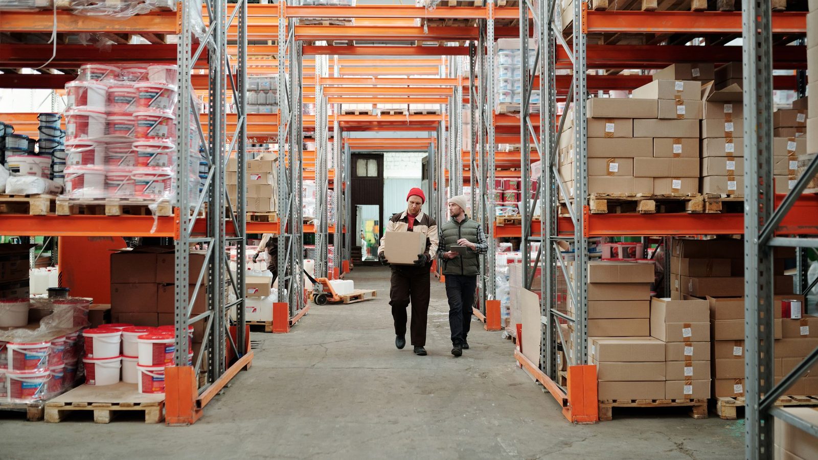 Two workers handle a package in a spacious warehouse surrounded by shelves stocked with boxes and products